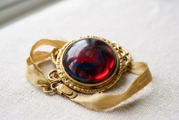 Collier vintage avec pendentif rond en cabochon rouge et bleu entouré d’un cadre doré travaillé, ruban satiné et petit tag signature. Bijoux Chanel vintage.